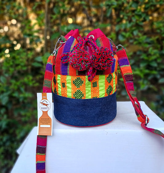 A beautiful handmade bucket bag made with red handwoven material and denim, embellished with cross stitch embroidery. With an adjustable strap and waterproof lining.