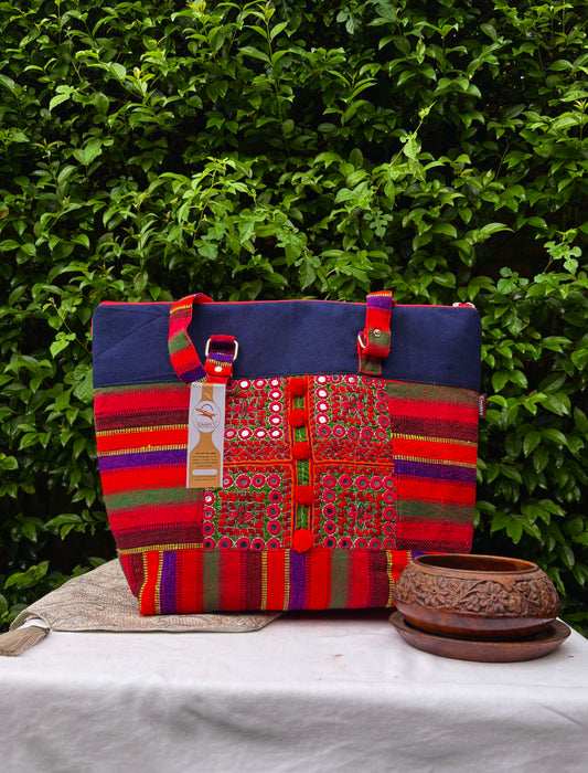 A colorful handmade tote bag with a navy blue denim top section and a highly detailed, multicolored embroidered and striped front panel. 